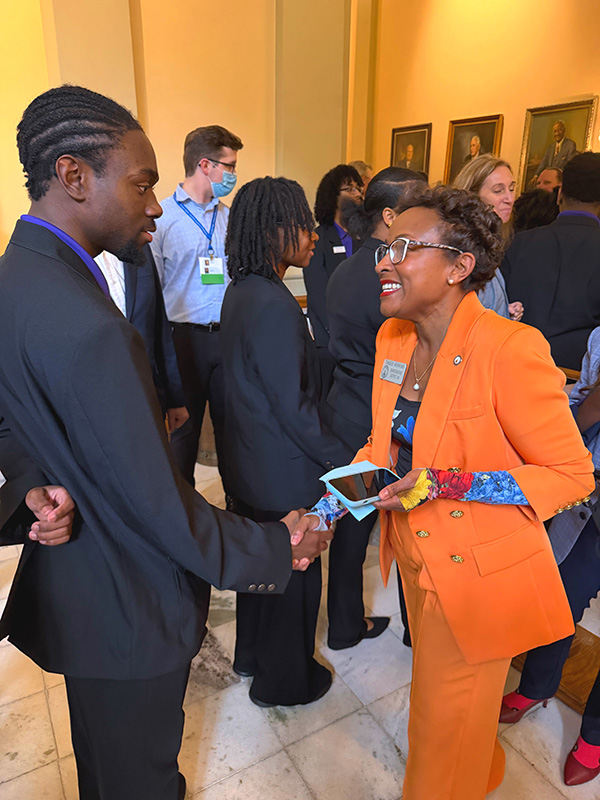 A representative in a vibrant orange suit shakes hands with a member of the President's Torch Society during their visit.